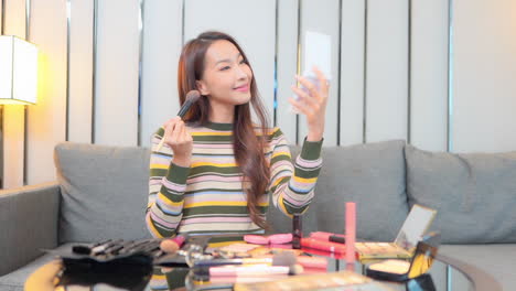 A-very-attractive-young-woman-with-makeup-spread-up-over-a-coffee-table-applies-makeup-to-her-flawless-skin