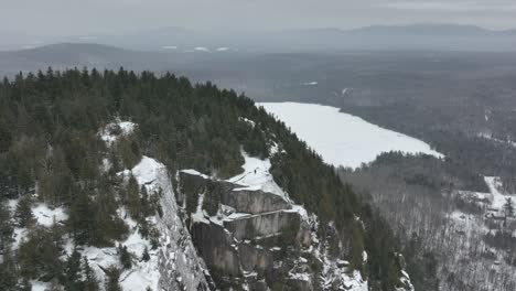 Aerial-Shot-Of-Man-On-Top-Of-A-Rocky-Winter-Mountains-In-Quebec,-Canada