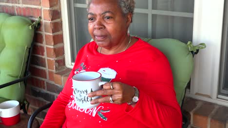 Happy-mature-African-American-black-woman-holding-a-hot-steaming-tea-or-coffee-cup-sitting-on-deck-on-a-chilly-winter-day