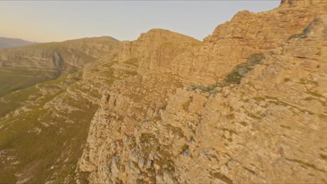 Beautiful,-spectacular-long-aerial-shot-approaching-a-mountain-and-then-flying-down-towards-the-coast-of-Cape-Town-at-sunset-at-high-speed