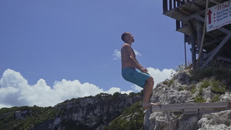 Young-man-does-backflip-off-cliff-ledge-into-stunning-blue-water,-slow-motion