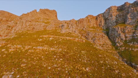 Spectacular-aerial-shot-of-pristine-forests,-hills-and-mountains-against-a-blue-sky,-turning-180-degrees-to-show-Cape-Town-at-sunset