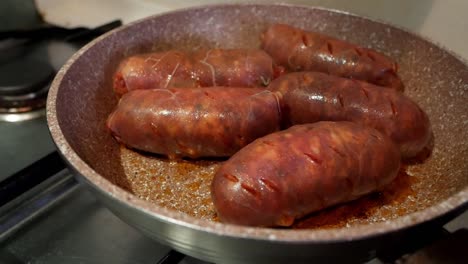 Five-big-and-bright-red-chorizo-sausages-being-cooked-in-a-pan