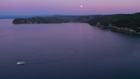 Boat-cruising-in-calm-Piran-bay-during-sunset,-aerial