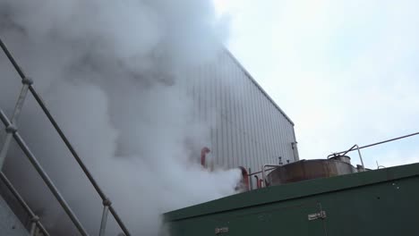 Heavy-steam-from-factory-boiler,-industrial-chimney-smoke---low-angle-static-shot