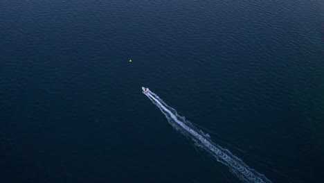 Speed-boat-cruising-past-shore-of-Piran-village,-aerial