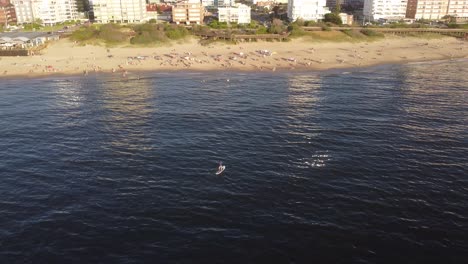 Aerial-orbiting-around-person-on-sup-board-paddling-over-sea-waters-along-Punta-del-Este-beach,-Uruguay