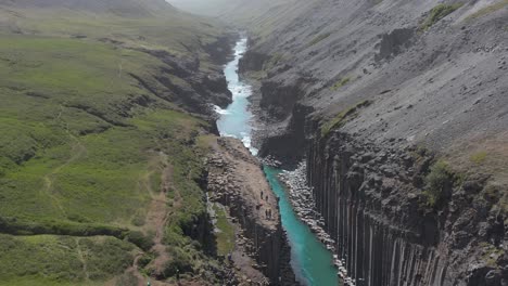 Famous-tourist-destination-Stuðlagil-with-bright-sunlight,-turquoise-glacial-water,-aerial