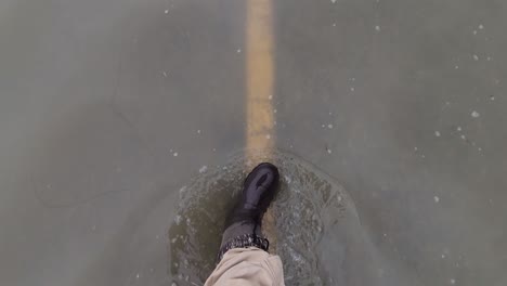 A-man-walking-on-a-flooded-automobile-road,-water-reaching-his-ankles
