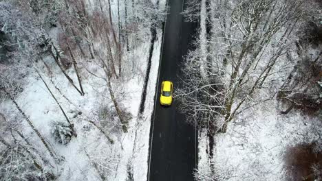 Beautiful-snowy-nature,-yellow-car-driving-through-a-winter-forest