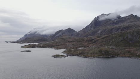 Aerial-drone-view-of-clouds-moving-over-steep-mountains,-dark,-autumn-day-in-Lofoten,-Norway