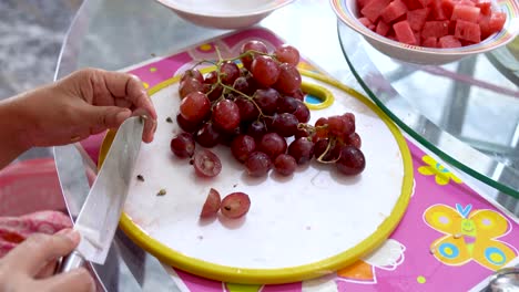 Female-preparing-fruit-dessert-is-cutting-grape-berries-and-removes-seeds,-close-up