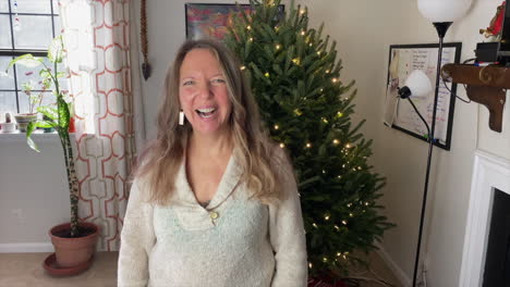 Mujer-Feliz-En-Casa-Se-Ríe-Frente-A-La-Cámara-Con-Un-árbol-De-Navidad-Decorativo-En-Segundo-Plano