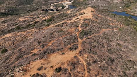 Aerial-drone-slow-motion-top-view-of-the-Calavera-hills-in-Carlsbad-California-and-the-coast-homes-living-by-the-side-of-the-coastline,-area-offers-6+-miles-of-dirt-biking-and-hiking-trails
