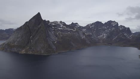 Aerial-view-of-steep-peaks-with-snow,-in-cloudy,-Lofoten,-Norway---pan,-drone-shot