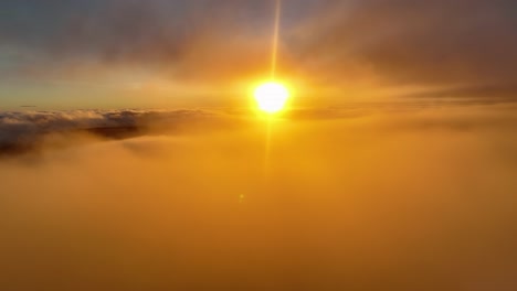 Sun-glowing-through-the-foggy-cloudscape,-Aerial-view-orange-setting
