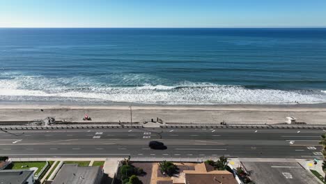 Aerial-from-left-to-right-of-the-beautiful-beach-in-Carlsbad-California,-USA-and-coast-highway-with-cars-passing-by-beside-the-Beach-on-a-town-landscape