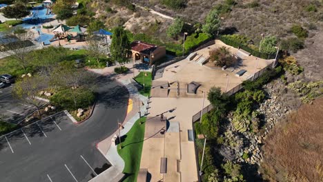 Aerial-view-of-outdoor-concrete-skate-park-with-ramps-and-pipes-with-a-guy-skateboarding-in-Alga-Norte-Park,-Carlsbad,-California-in-USA