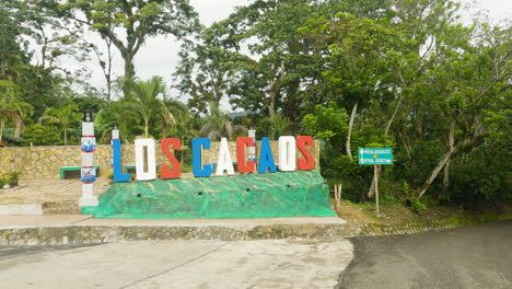 Dolly-in-towards-colorful-Los-Cacaos-town-sign,-Dominican-Republic,-day