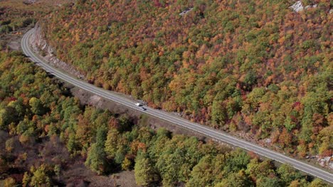 Car-driving-on-rural-road-through-autumn-season-forest,-aerial