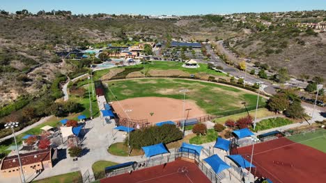 Aerial-view-of-a-baseball-field-and-drone-flying-backwards-to-a-football-ground-at-Alga-Norte-Park,-Carlsbad,-California