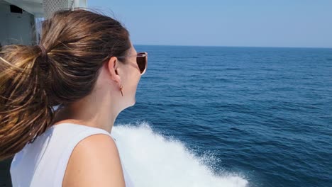 Schöne-Junge-Frau-Im-Boot-Mit-Sonnenbrille-Posiert-Und-Lächelt-In-Die-Kamera,-Während-Sie-Im-Ozean-Segelt