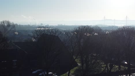 Frosty-mist-surrounding-urban-British-town-house-rooftops-aerial-view-early-morning-rising-pan-left-across-park-trees