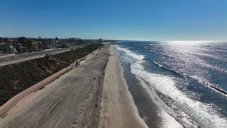 Aerial-view-over-the-waves-crashing-against-the-shoreline-along-the-beaches-of-Carlsbad,-California,-USA-with-sunlight-falling-on-the-sea-water