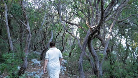 Back-View-Of-A-Woman-In-White-Dress-Walking-Through-The-Forest-Towards-The-Emplisi-Beach-In-Greece