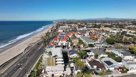 Aerial-shot-from-right-to-left-over-the-beautiful-beach-of-Carlsbad-California,-USA-and-Coast-Highway-with-cars-passing-by-beside-the-Beach-on-a-town-landscape