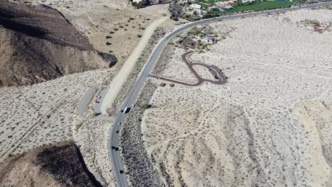 Desert-highway-leading-towards-small-town-with-green-grass,-high-altitude-drone-shot