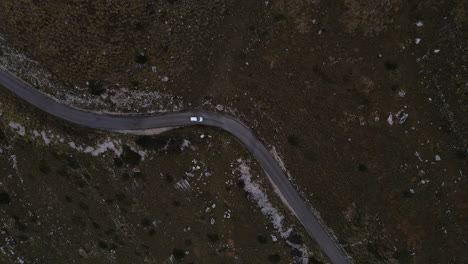 Drone-shot-of-car-driving-through-the-mountains-with-rocks-in-Montenegro