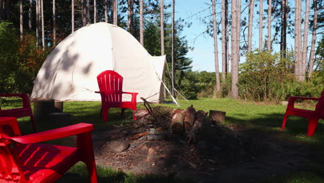 Ein-Paar-Rote-Plastikstühle-Stehen-Neben-Einem-Lagerfeuer-Im-Wald,-Wo-Im-Hintergrund-Ein-Zelt-Aufgestellt-Ist