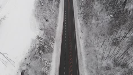 Flying-Over-Asphalt-Road-In-Winter-Forest---aerial-drone-shot