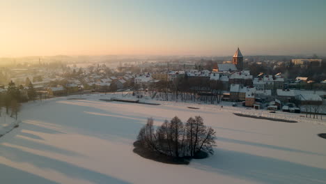 Atemberaubender-Sonnenaufgang-über-Der-Verschneiten-Landschaft-In-Gorowo-Ilaweckie,-Nordpolen-Mit-Weitem-Blick-Auf-Die-Gotische-Kirche-Im-Winter