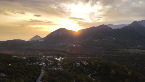 Beautiful-aerial-drone-shot-of-sunrise-over-the-mountain-range-with-the-view-of-a-small-town-at-the-foothills-of-the-range-in-Montenegro