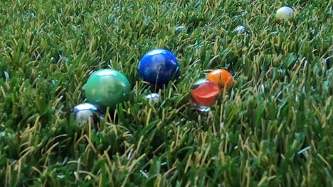 Close-up-of-marbles-being-thrown-onto-a-thick-green-grass