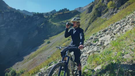 Ein-Mountainbiker-Trinkt-Aus-Seiner-Wasserflasche,-Umgeben-Von-Hohen-Bergen