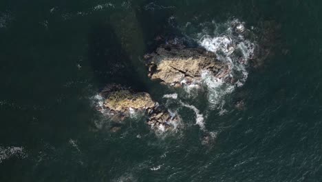 Aerial-view-of-waves-crashing-into-two-large-rocks-in-Manuel-Antonio-Beach-In-Quepos,-Costa-Rica,-Top-down-wide-shot