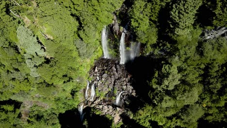 Close-up-of-a-double-waterfall-with-a-rainbow-hidden-in-the-middle-of-the-forest---aerial