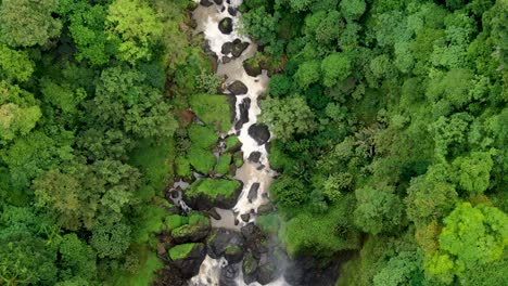 Small-waterfall-streams-through-green-forest,-forward-overhead-aerial