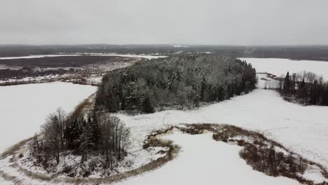 Aerial-drone-view-of-a-snowy-meadow-next-to-frozen-lakes-in-winter