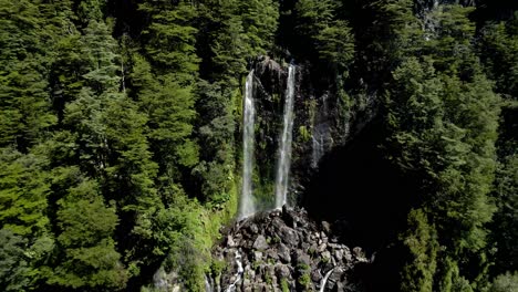 Reverse-view-of-the-waterfall-la-nina-encantada-hidden-in-a-forest-in-southern-chile---dolly-out-drone-shot