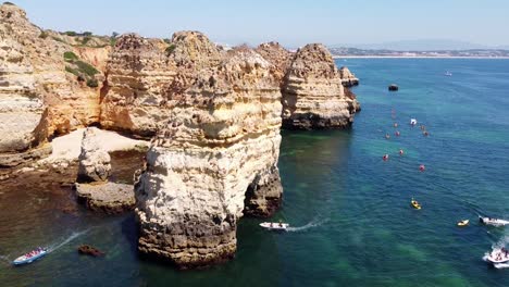 Ponta-Da-Piedade,-Lagos,-Algarve---Aerial-Drone-View-with-Boats,-Kayaks,-Rocky-Cliffs,-Beautiful-Coastline-and-Clear-Blue-Sea