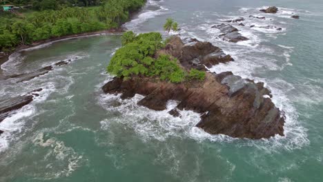 Aerial-of-foamy-turquoise-sea-weaves-near-rocky-shore-covered-in-vegetation-in-Dominicalito-Beach,-Costa-Rica