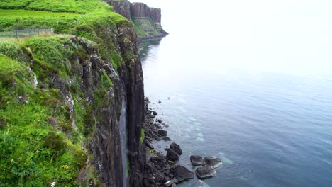 Waterfall-over-the-verdant-cliff-edge-down-into-the-Mealtfalls-into-the-clear-blue-waters-as-a-bird-flies-away