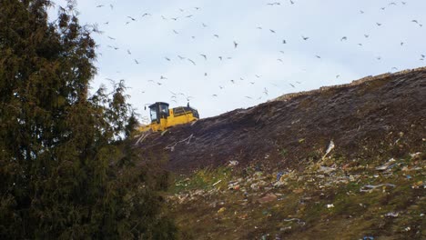 Stack-of-different-types-of-large-garbage-dump,-plastic-bags,-and-landfill-full-of-trash,-environmental-pollution,-yellow-truck-dump-waste-products-polluting-in-a-dump,-distant-wide-shot