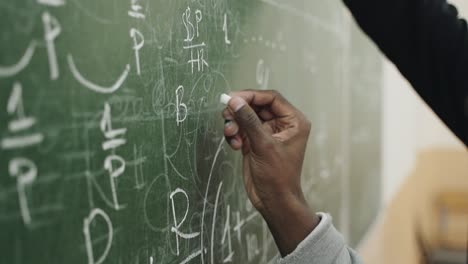 Close-up-shot-of-young-man-writing-solution-of-equation-on-greenboard-at-school-during-math-lesson-with-professor