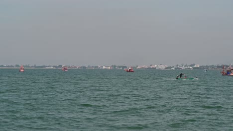A-speeding-fishing-boat-towards-the-right-while-others-anchored-during-a-sunny-lovely-day-and-the-background-is-the-city-of-Pattaya-in-Chonburi,-Thailand