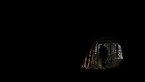 A-man-opens-the-gate-and-walks-into-a-dark-tunnel,-backlit-anonymous-footage-with-copy-space